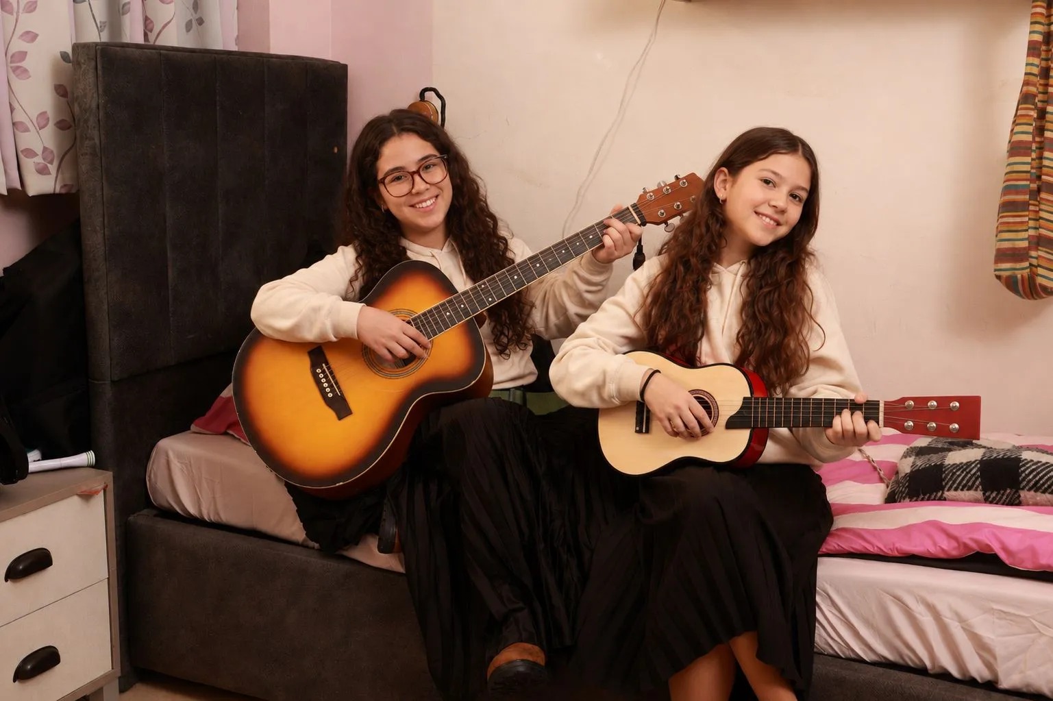 Two girls playing guitars together in their room